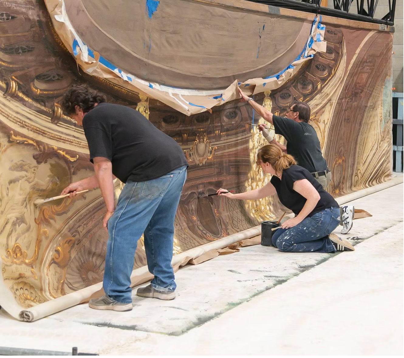 Michael Denering, Karen Maness, and Joe Francuz repair an MGM backdrop from <i>The Law and the Lady</i> (1951). Conservation work such as cleaning, stabilization, and repair helps preserve historic Hollywood scenic art for research, exhibition, and public interpretation.
